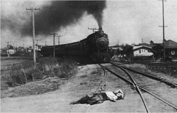 A black and white film still of a woman tied to train tracks as a locomotive approaches